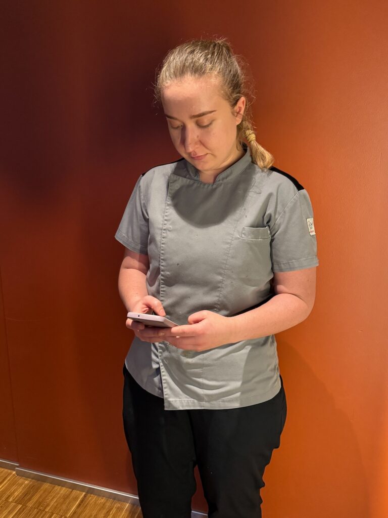 a woman in a grey shirt, working on a smartphone